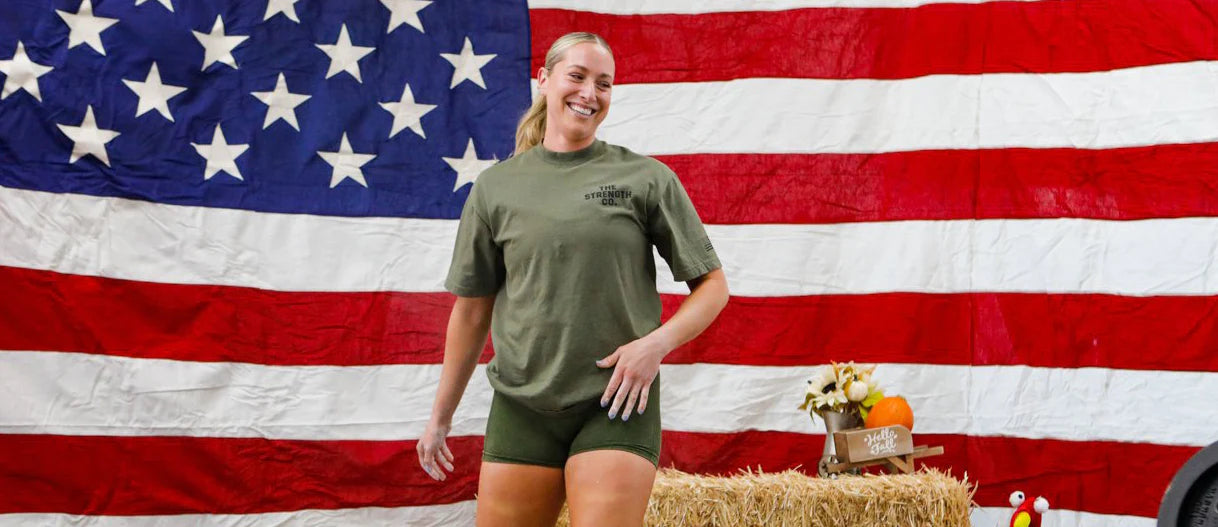 A woman wearing a The Strength Co. shirt with an American flag in the background
