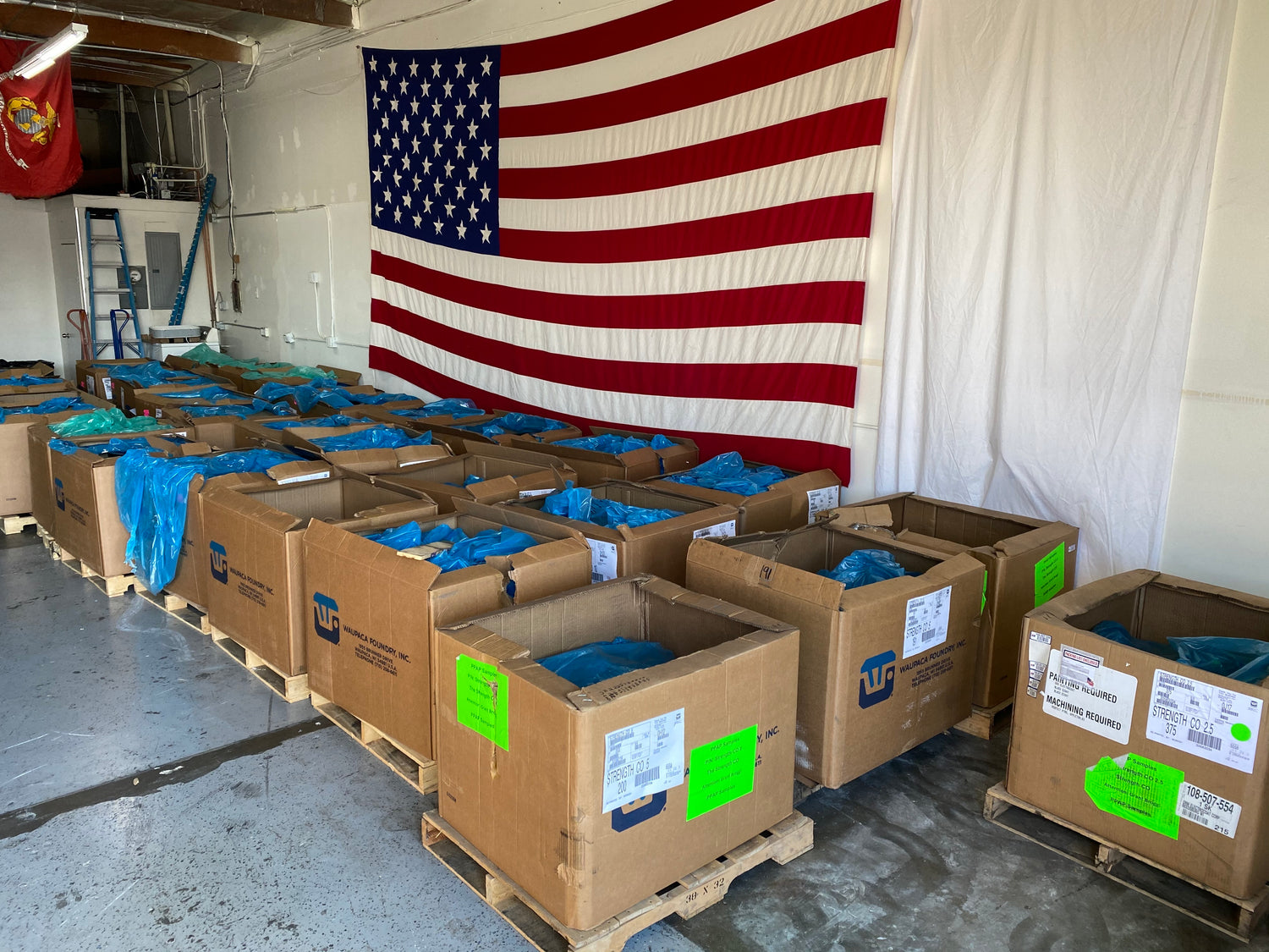 Pallets of Made-in-USA Strength Co. plates beneath the American flag